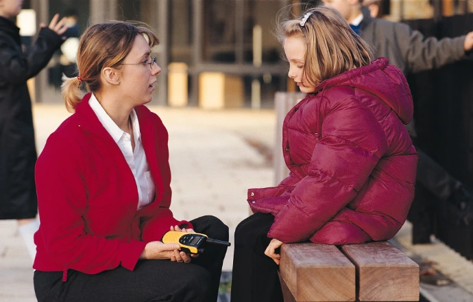 A teacher holding a two-way radio, talking to a pupil, in a playground